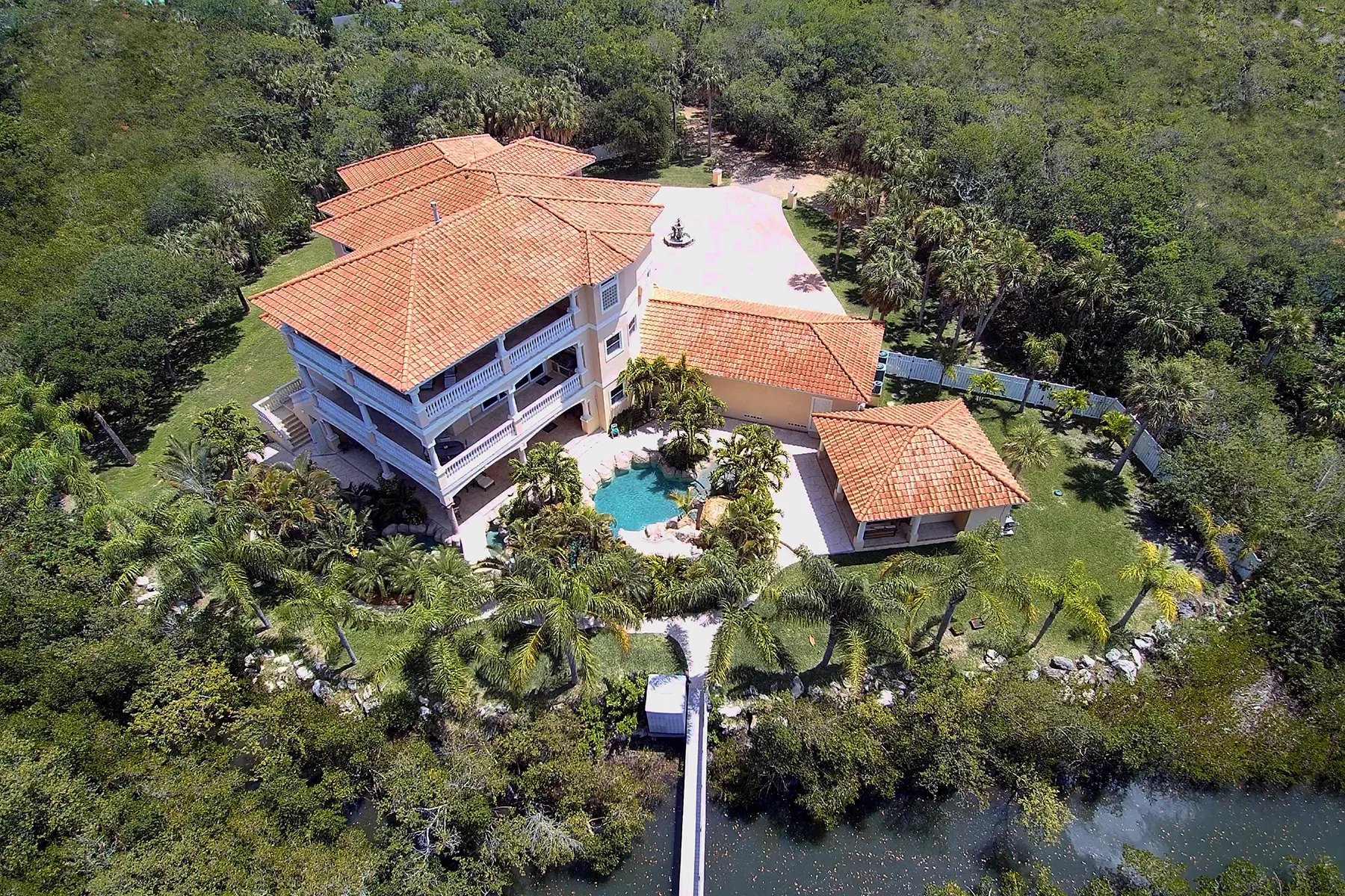 Aerial view of a home with a pool, mature trees, and a waterside dock.
